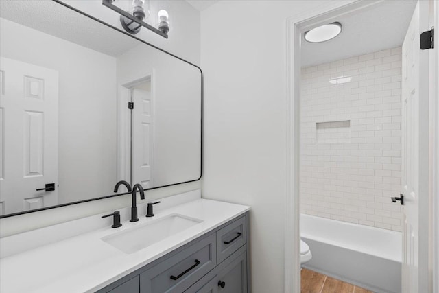 full bathroom with tiled shower / bath, hardwood / wood-style floors, vanity, toilet, and a textured ceiling