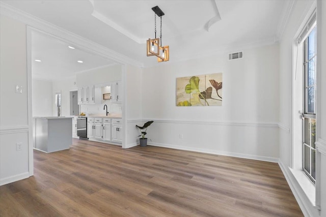 unfurnished dining area with ornamental molding, sink, hardwood / wood-style floors, and an inviting chandelier