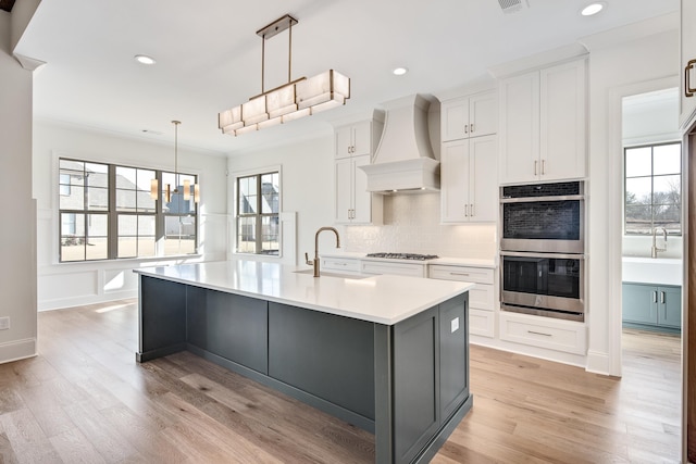 kitchen featuring stainless steel double oven, a sink, white cabinets, and custom range hood