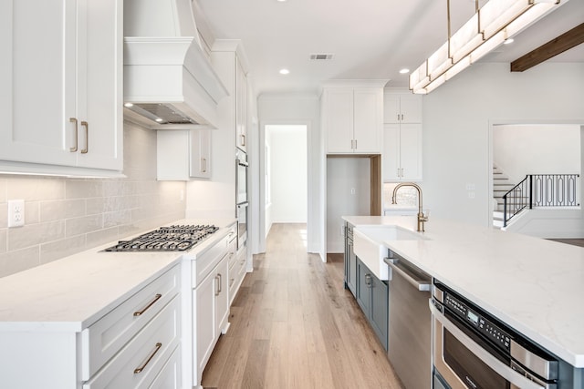 kitchen with light wood finished floors, white cabinets, decorative backsplash, custom range hood, and appliances with stainless steel finishes