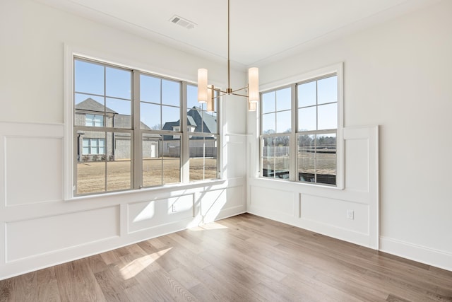 unfurnished dining area with visible vents, a decorative wall, an inviting chandelier, wood finished floors, and baseboards