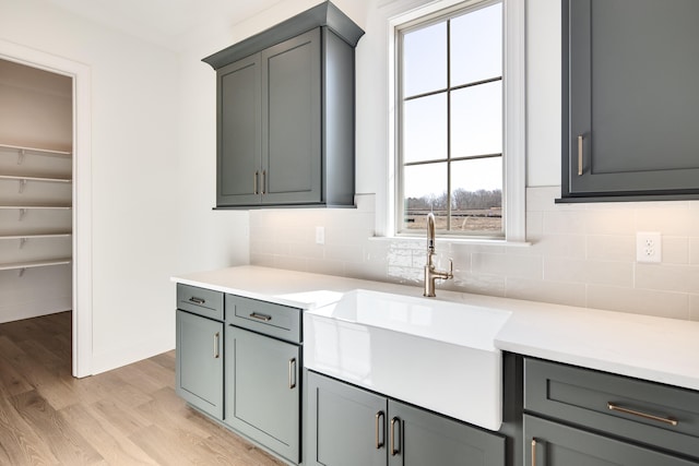 kitchen with tasteful backsplash, light wood-type flooring, light countertops, and a sink