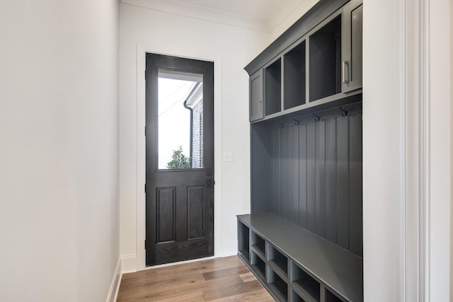 mudroom with baseboards, crown molding, and light wood-style floors