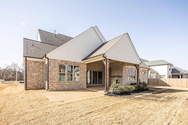 rear view of house with brick siding, a patio area, fence, and a shingled roof