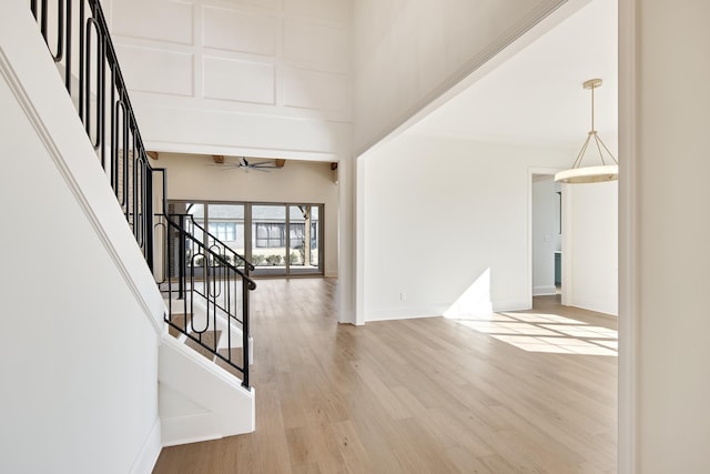 interior space with ceiling fan, a high ceiling, wood finished floors, baseboards, and stairway