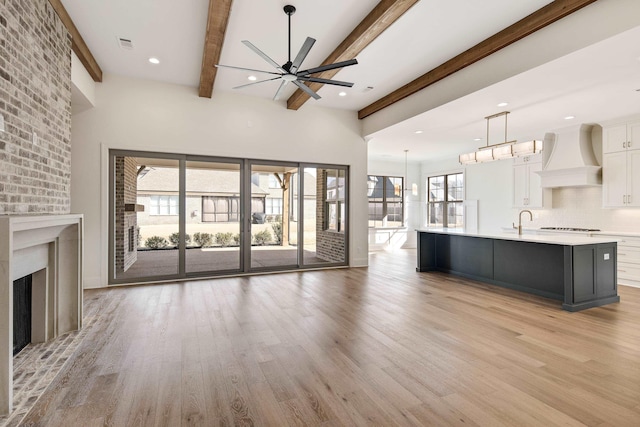 unfurnished living room featuring light wood-style floors, a fireplace, a ceiling fan, and beam ceiling