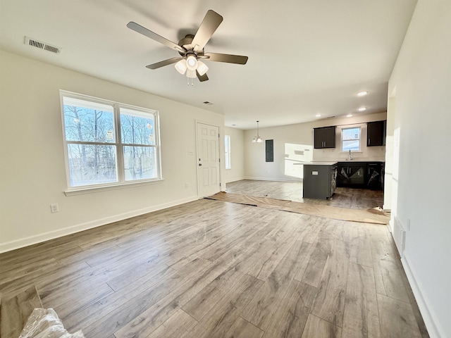 unfurnished living room with visible vents, light wood-style floors, a sink, ceiling fan, and baseboards