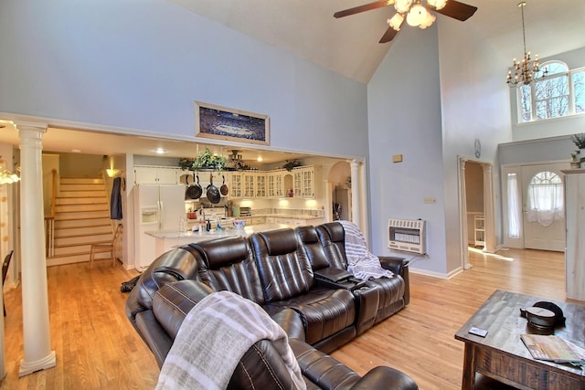 living room with ornate columns, ceiling fan with notable chandelier, heating unit, high vaulted ceiling, and light hardwood / wood-style flooring