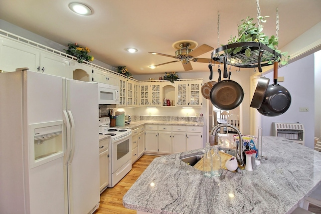 kitchen with sink, heating unit, light stone counters, light hardwood / wood-style flooring, and white appliances