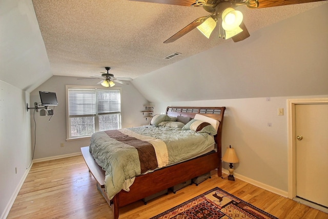 bedroom featuring lofted ceiling, a textured ceiling, light hardwood / wood-style floors, and ceiling fan