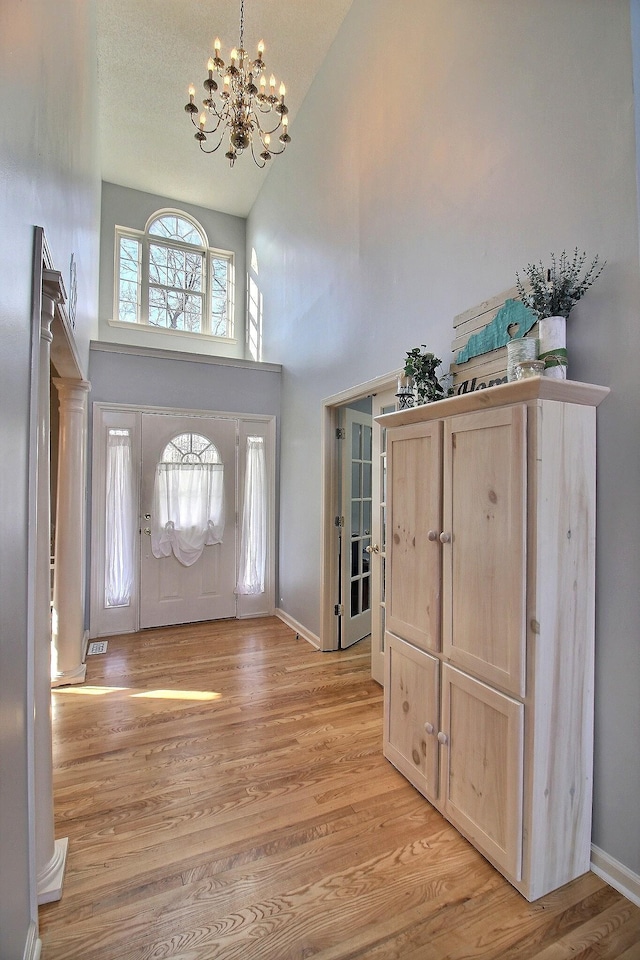 foyer entrance with an inviting chandelier, high vaulted ceiling, and light hardwood / wood-style flooring