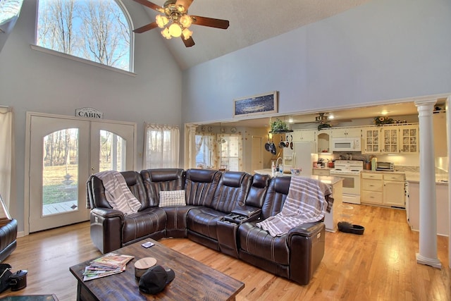 living room with ornate columns, ceiling fan, light wood-type flooring, and high vaulted ceiling