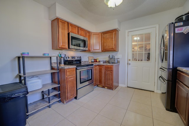 kitchen featuring appliances with stainless steel finishes, light tile patterned floors, and a textured ceiling