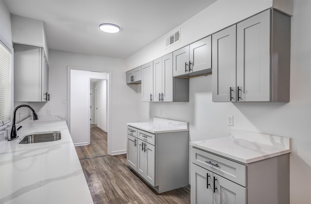 kitchen featuring dark hardwood / wood-style floors, light stone countertops, sink, and gray cabinetry