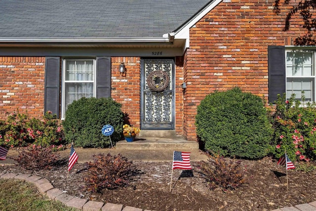 view of exterior entry with brick siding and roof with shingles