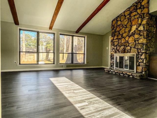 unfurnished living room featuring a stone fireplace, plenty of natural light, lofted ceiling with beams, and dark hardwood / wood-style floors