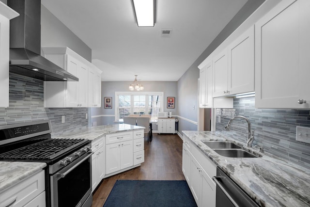 kitchen featuring stainless steel gas stove, sink, white cabinets, hanging light fixtures, and wall chimney range hood