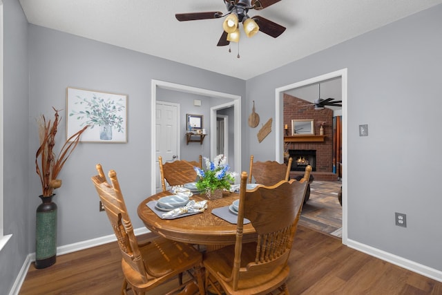 dining area with a brick fireplace, dark hardwood / wood-style floors, and ceiling fan