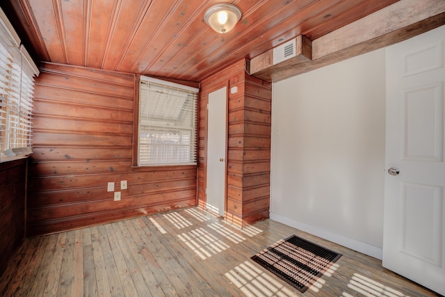 empty room featuring a wealth of natural light, light hardwood / wood-style flooring, wooden ceiling, and wood walls