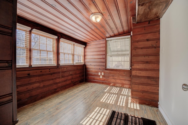 empty room featuring vaulted ceiling, wooden walls, wooden ceiling, and light wood-type flooring