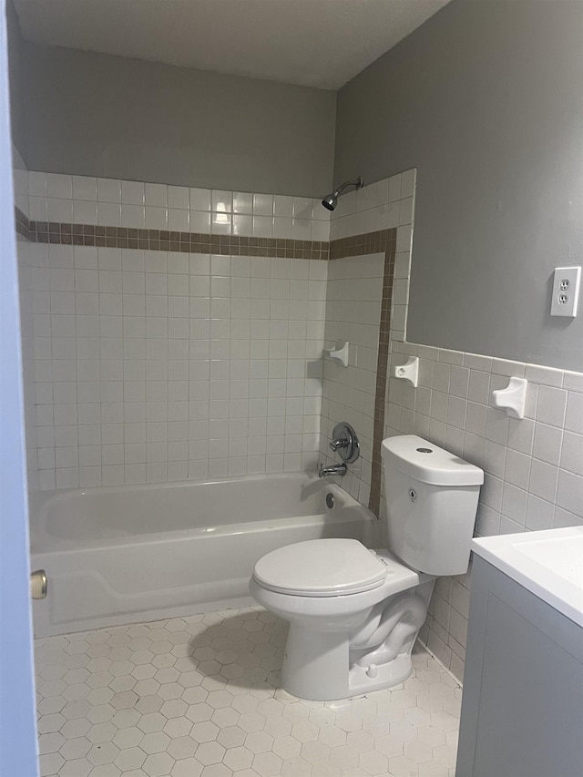 full bathroom with tile patterned floors, toilet, tiled shower / bath, tile walls, and vanity