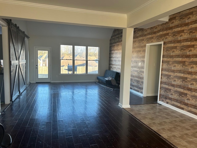 empty room with dark wood-style floors, a barn door, ornamental molding, and baseboards