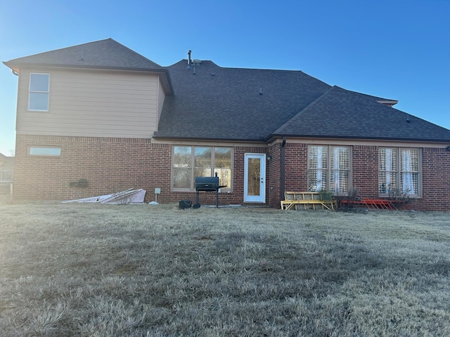 back of property featuring a yard, a shingled roof, and brick siding