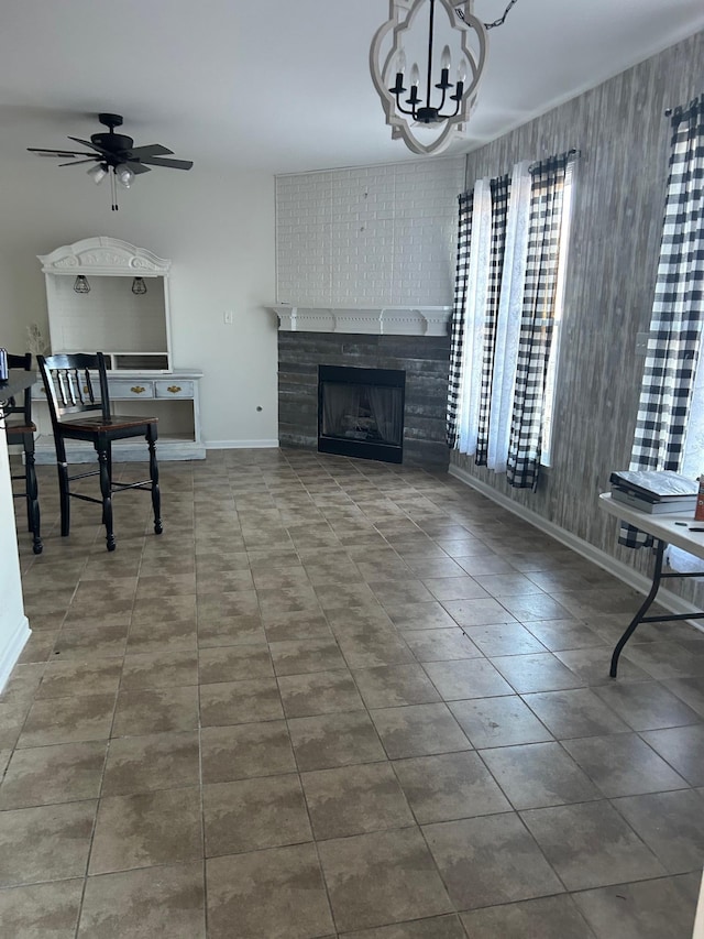 tiled living room featuring a fireplace, baseboards, and ceiling fan with notable chandelier