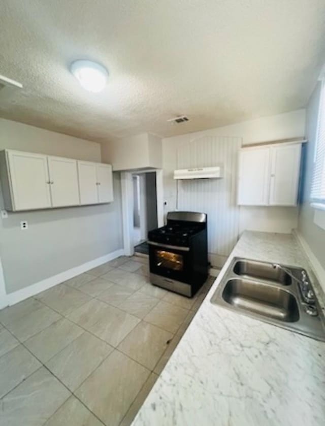 kitchen with sink, white cabinets, light tile patterned floors, stainless steel range with gas stovetop, and a textured ceiling