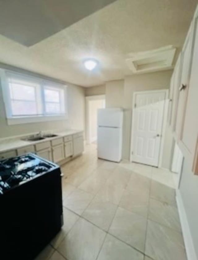 kitchen featuring black range oven, sink, white fridge, and light tile patterned floors