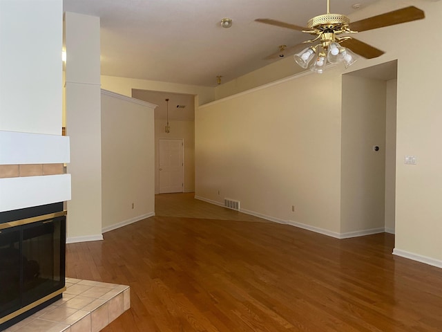 unfurnished living room with a tiled fireplace, wood-type flooring, and ceiling fan