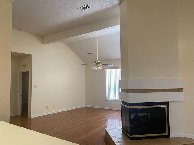 unfurnished living room with vaulted ceiling with beams, a textured ceiling, a multi sided fireplace, ceiling fan, and hardwood / wood-style floors