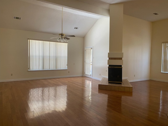 unfurnished living room featuring beam ceiling, light wood-type flooring, a tile fireplace, and a wealth of natural light