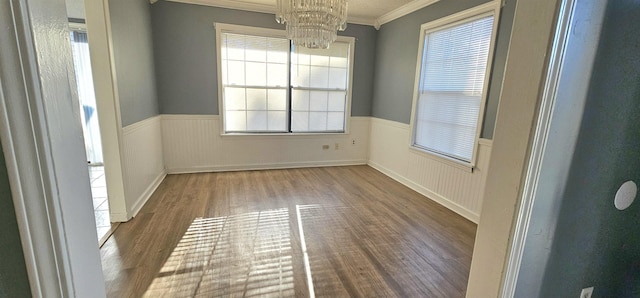 spare room with an inviting chandelier, wood-type flooring, and ornamental molding