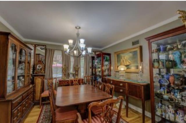 dining room with ornamental molding, an inviting chandelier, and light wood-type flooring