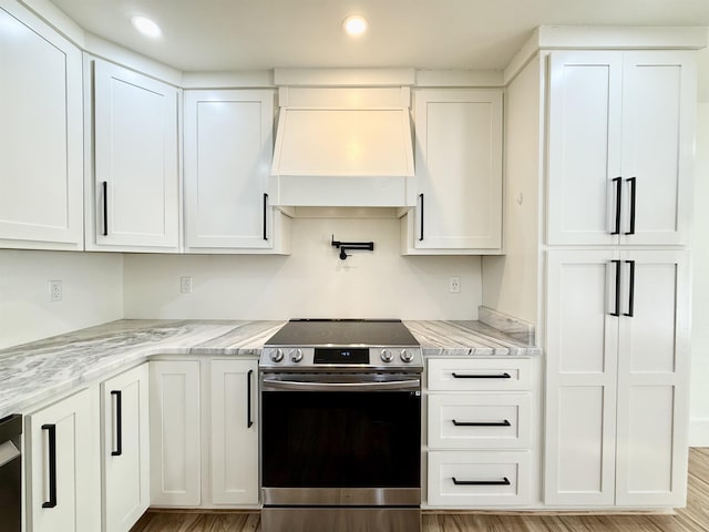 kitchen with light stone counters, stainless steel electric stove, custom range hood, and white cabinets