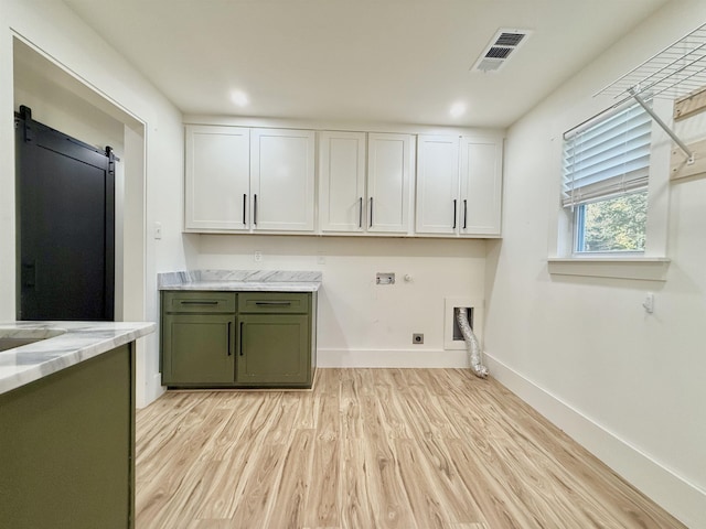 clothes washing area featuring cabinets, light hardwood / wood-style flooring, hookup for an electric dryer, washer hookup, and a barn door