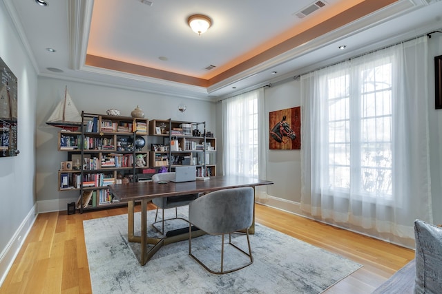 home office featuring crown molding, a tray ceiling, light hardwood / wood-style floors, and a healthy amount of sunlight