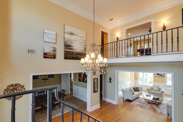 staircase with a high ceiling, crown molding, hardwood / wood-style floors, and a notable chandelier