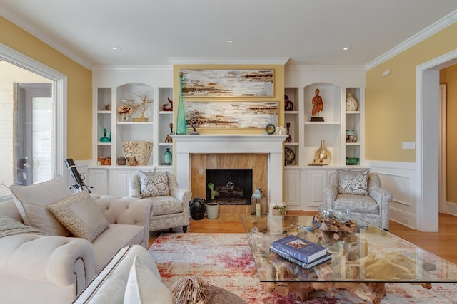 living area featuring built in shelves, ornamental molding, light hardwood / wood-style floors, and a tile fireplace