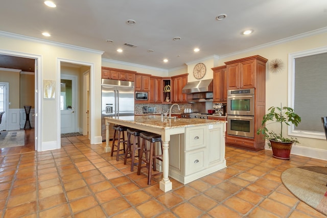 kitchen featuring backsplash, a kitchen breakfast bar, a kitchen island with sink, built in appliances, and crown molding