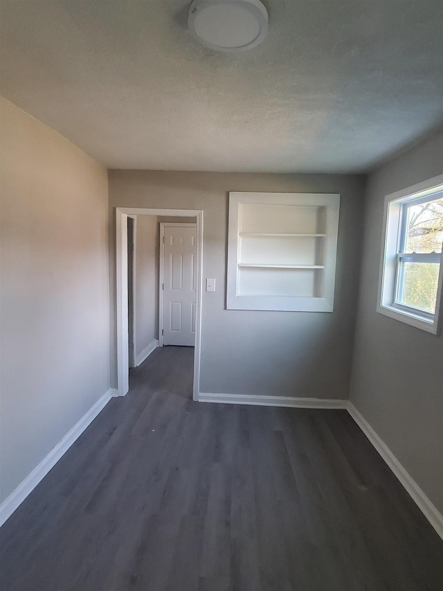 spare room with built in shelves, dark hardwood / wood-style floors, and a textured ceiling