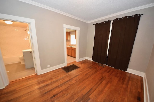 unfurnished bedroom featuring sink, ensuite bathroom, wood-type flooring, ornamental molding, and a textured ceiling