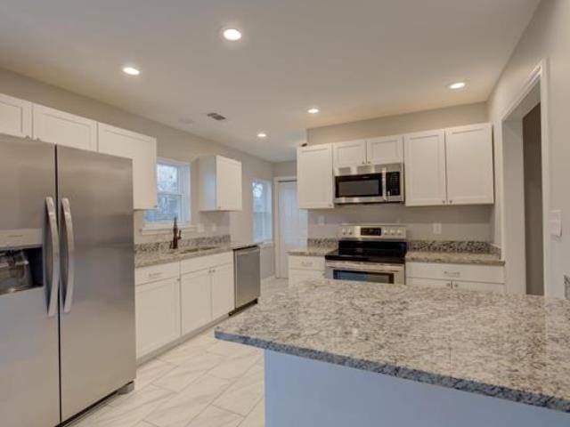 kitchen with stainless steel appliances, light stone countertops, sink, and white cabinets