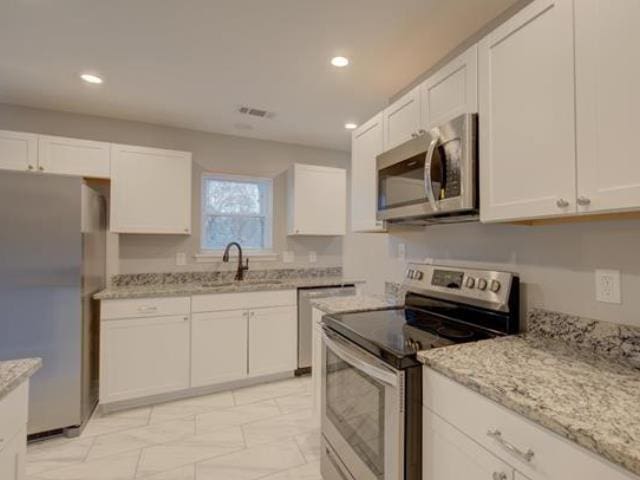 kitchen featuring stainless steel appliances, white cabinetry, light stone countertops, and sink