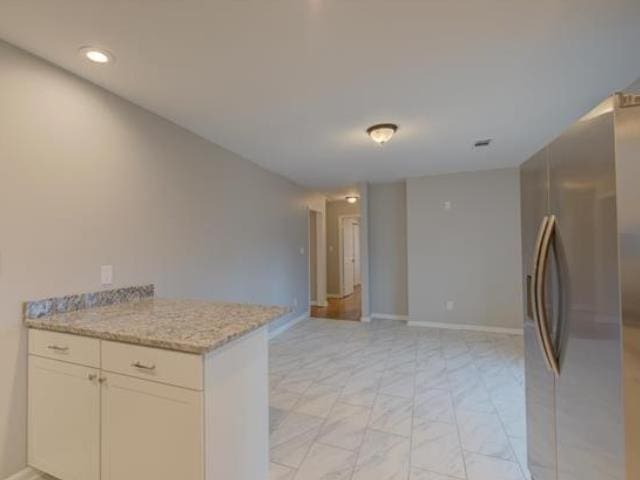 kitchen featuring white cabinetry, light stone counters, and stainless steel refrigerator with ice dispenser