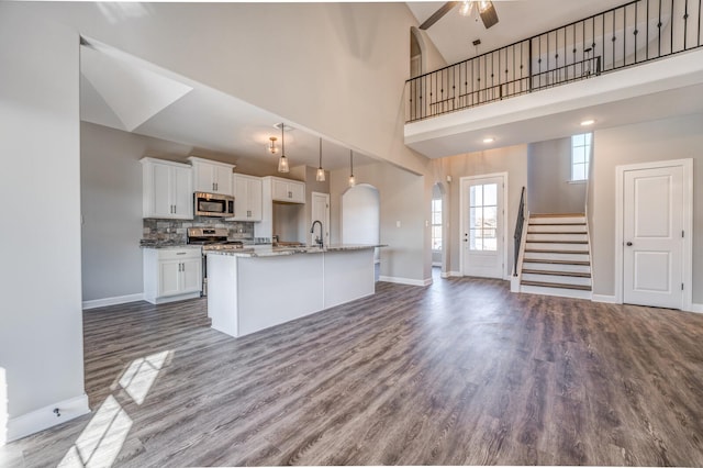 kitchen featuring white cabinetry, wood-type flooring, appliances with stainless steel finishes, an island with sink, and a towering ceiling