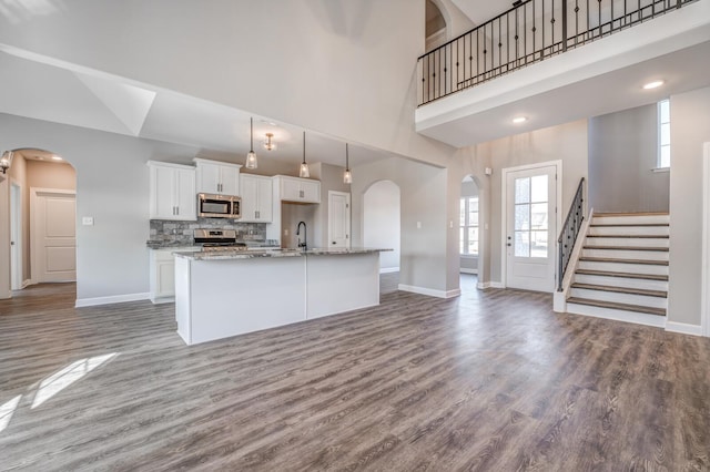 kitchen with appliances with stainless steel finishes, a high ceiling, white cabinets, a center island with sink, and decorative backsplash