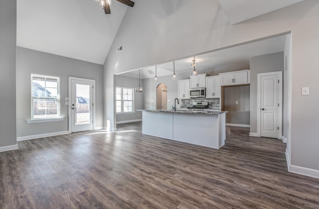 kitchen with appliances with stainless steel finishes, white cabinetry, a kitchen island with sink, light stone counters, and decorative light fixtures