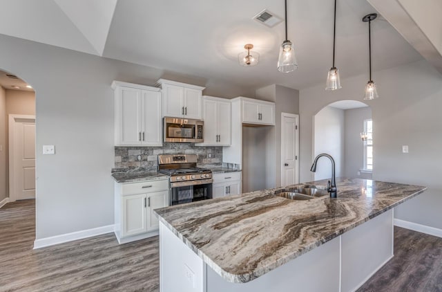 kitchen featuring decorative light fixtures, sink, white cabinets, stainless steel appliances, and a center island with sink